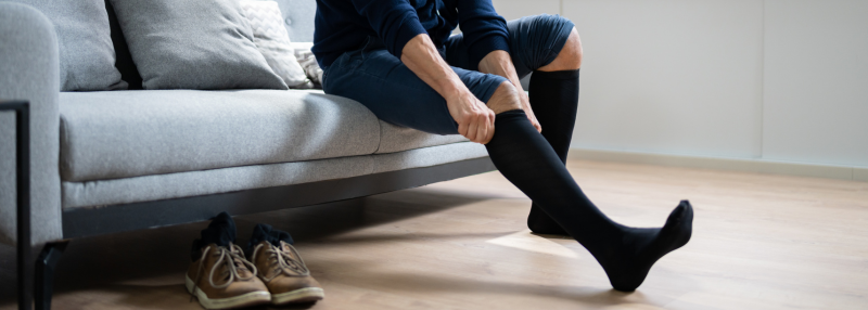 Man sitting on the couch and pulling on black compression socks