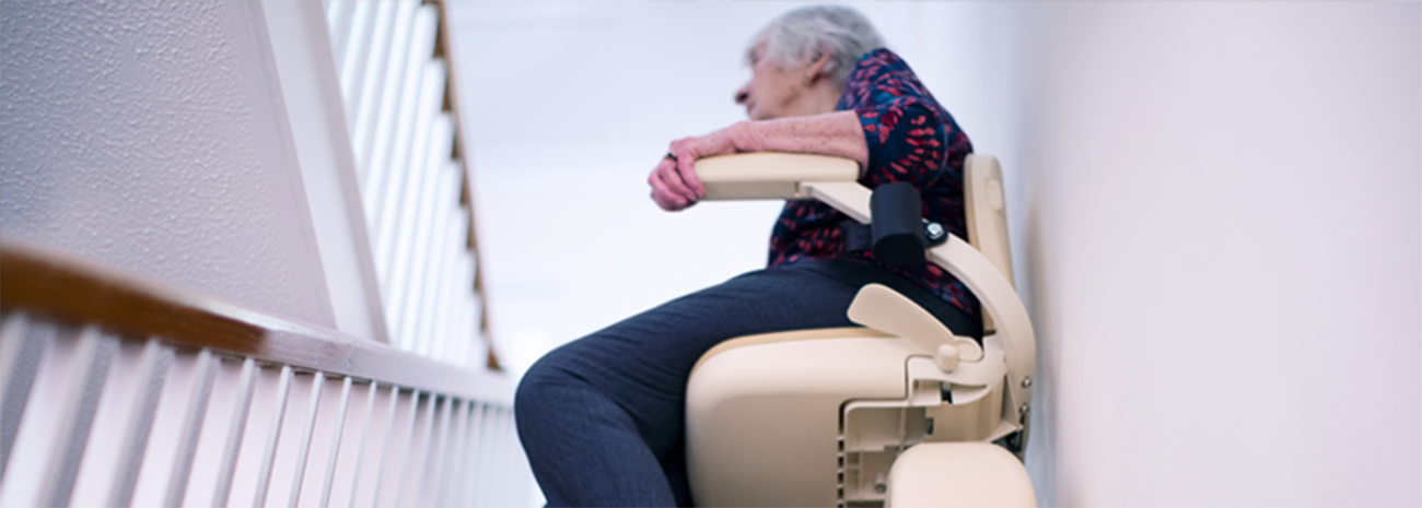 Senior woman sitting in beige stair lift and going up the stairs in her house