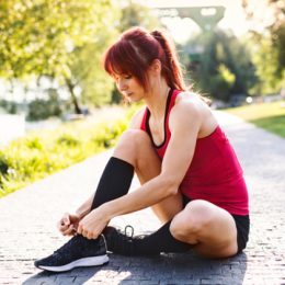 Woman sitting on ground adjusting running shoes while wearing compression socks