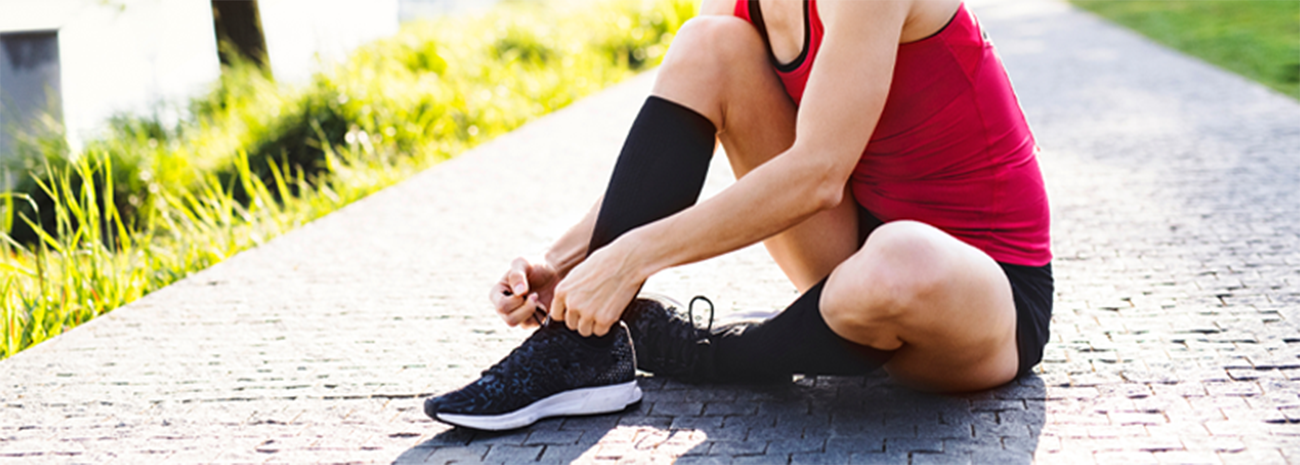 Woman sitting on ground adjusting running shoes while wearing compression socks