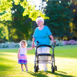 Happy senior lady with a walker rollator and a toddler girl walking together in the park in summertime