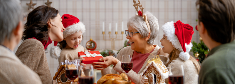 Grandmother and granddaughter exchanging gift with family around the table during Christmas