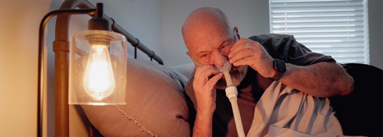 Man putting a CPAP nasal mask on his face while lying in bed