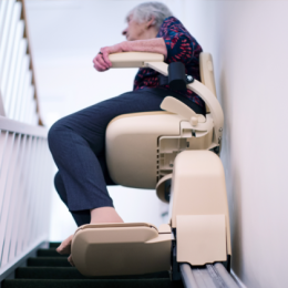 Senior woman sitting in beige stair lift and going up the stairs in her house