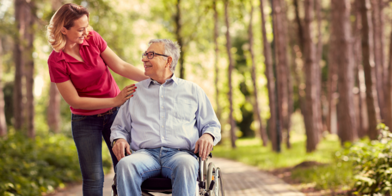 Photo of a woman walking outside with an older man in a wheelchair.