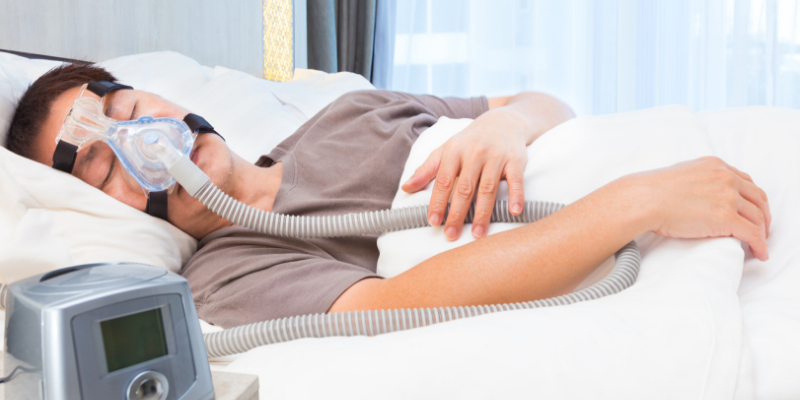 Photo of a man sleeping with a CPAP mask on and his CPAP machine next to him.