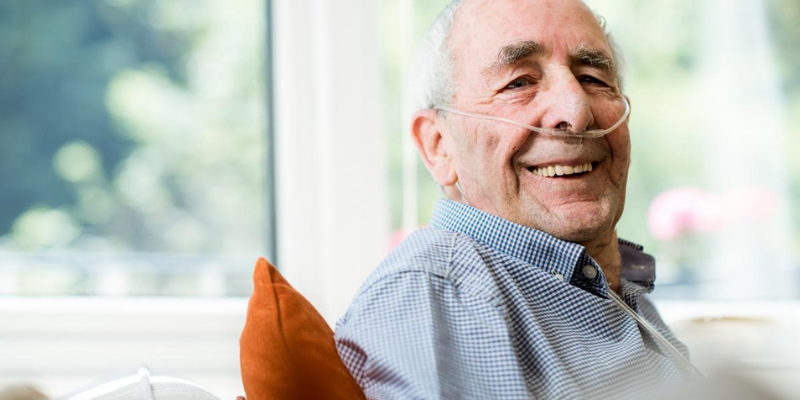 Photo of a man sitting inside with oxygen hooked up.