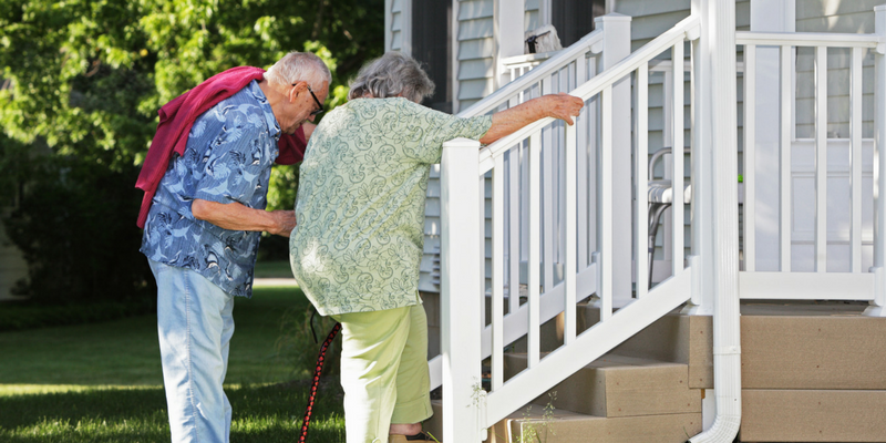 Photo of an elderly couple who is helping each other up the steps of their home.