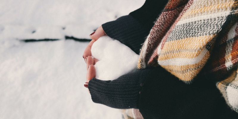 Photo of a person holding snow in their hands and the snow is shaped like a heart.