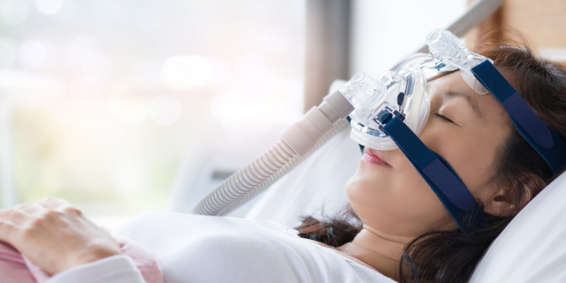 Photo of a woman lying down sleeping with a CPAP mask on her face.