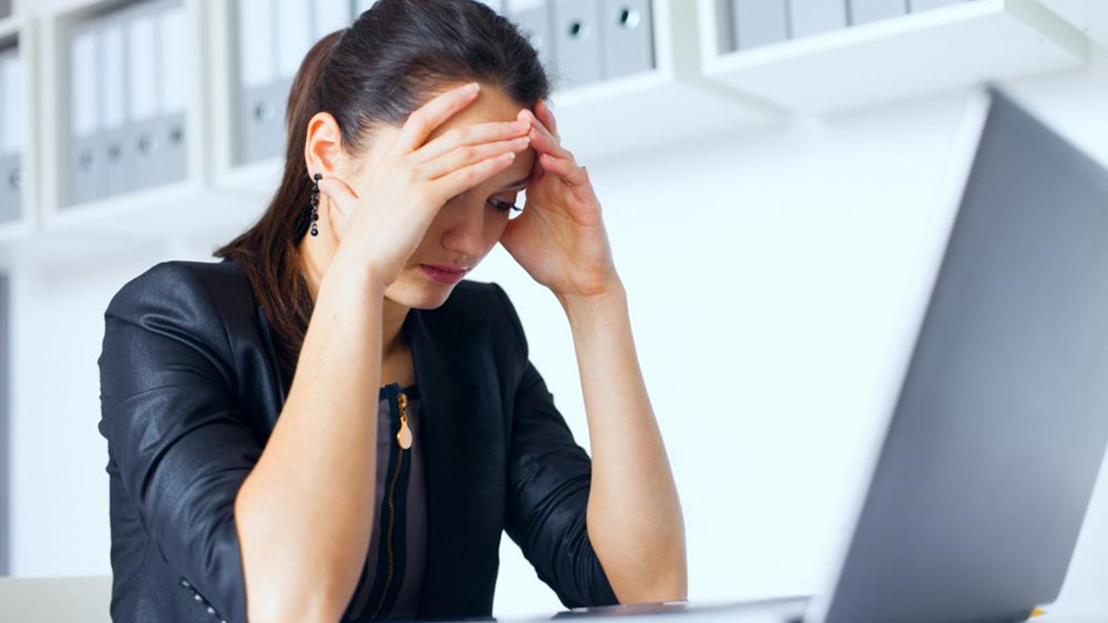 Woman sitting in front of her laptop with her hands on her face, looking stressed.