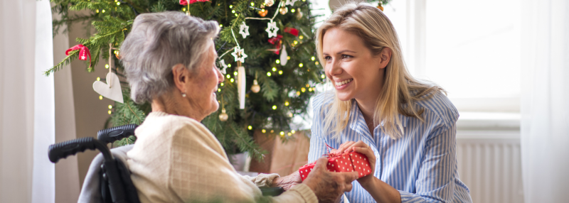 Daughter giving elderly mother in a wheelchair a Christmas gift