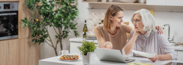 Adult daughter looking at the computer with her senior mom in the kitchen
