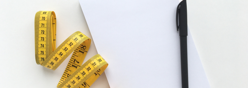 Measuring table in a spiral on a white table with a notepad and pen next to it