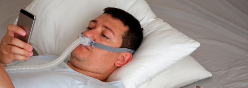 Man lying in bed with his CPAP mask on using his smartphone