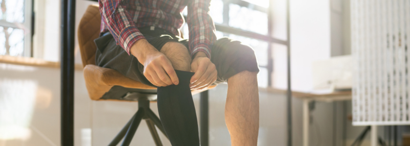 Man pulling on compression stockings while seated on a chair