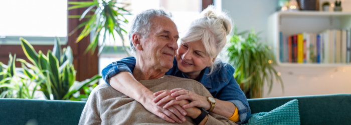 Happy senior couple with arms around each other on the couch in their home