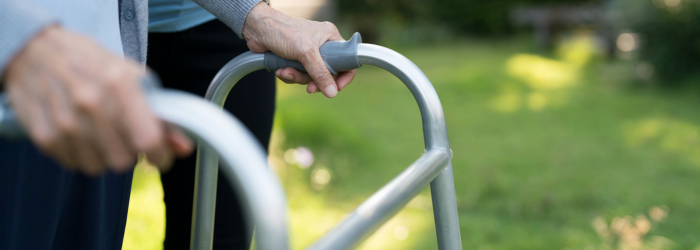 Senior woman using walker outdoors with caregiver or daughter next to her